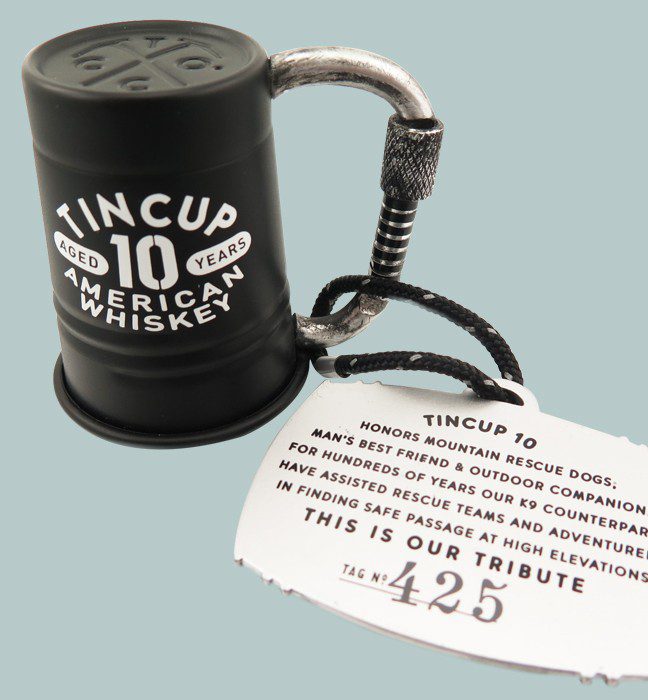 Close up photograph of a tin cup whiskey metallic embossed labels and usable cap closure, showcasing Cpg production feasible packaging created by a printing and design agency.