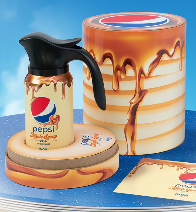 Photograph of an influencer unboxing experience promoting the limited edition IHOP x Pepsi maple syrup flavor, featuring a can of cola with a custom Pepsi Spout, inspired by the iconic IHOP syrup pitchers, and a customized note for influencers.